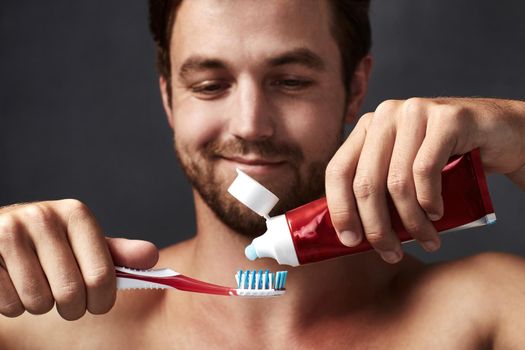 Remember to brush in the morning and night. a handsome young man putting toothpaste on his toothbrush.