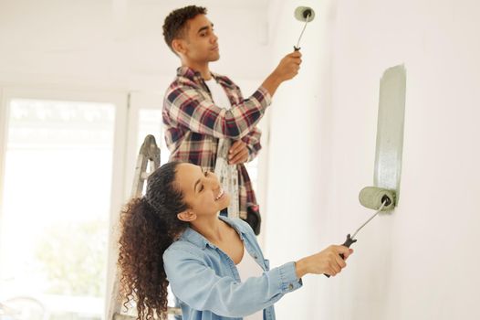 Painting, love and renovation with a couple doing DIY in a room for improvement and remodel of their home. Young man and woman working with green paint on a wall to renovate their domestic house