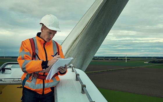 Making sure he has everything on his checklist. a young engineer inspecting a wind turbine.