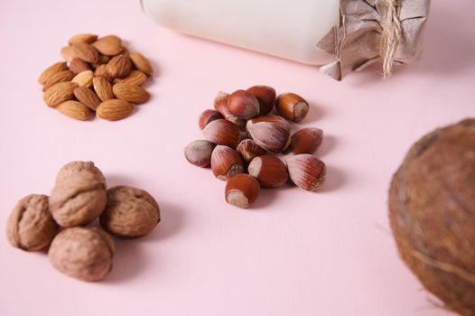 Focus on organic hazelnuts near assortment of wholesome nuts and a bottle of non dairy milk, isolated on pink background
