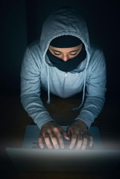 Hell crack that code. High angle shot of a man in a hoodie and mask hacking a computer network.