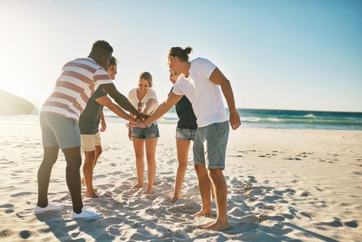 Summer for the win. a group of young joining their hands together in solidarity at the beach.