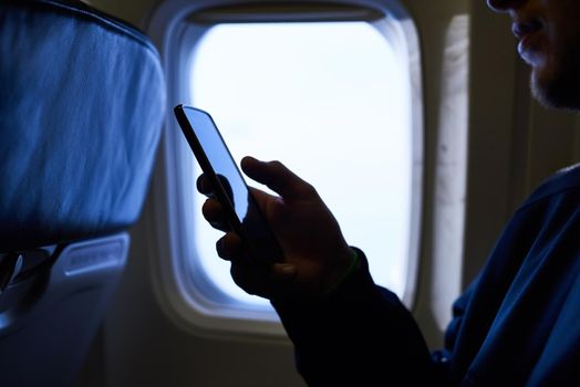 Switching his phone to airplane mode. an unidentifiable passenger using his cellphone inside an airplane cabin.