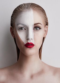 Dare to be different. a beautiful woman wearing face paint and red lipstick against a plain background.