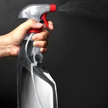 Spritz and spray. a person spraying from a bottle of detergent isolated on black.