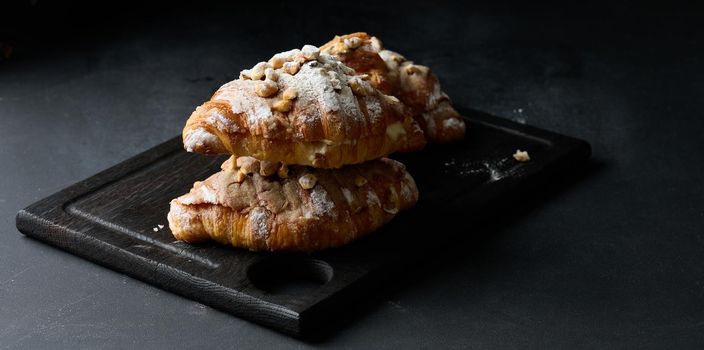 Baked croissant on a  board and sprinkled with powdered sugar, black table. Appetizing pastries for breakfast	