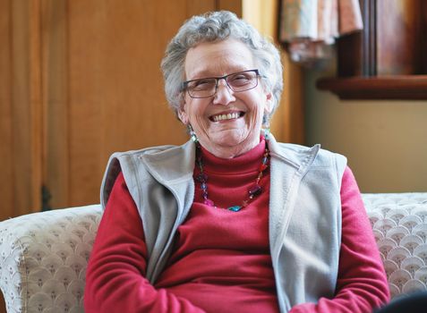 Happy elderly woman smiling sitting on sofa at home enjoying retirement