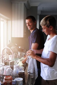 Families are about sharing respect and responsibility. a father and son cleaning dishes together at home.