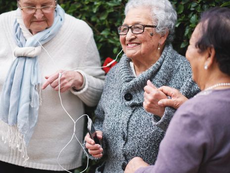 Happy old women listening to music on smartphone wearing earphones smiling enjoying fun celebrating retirement together outdoors