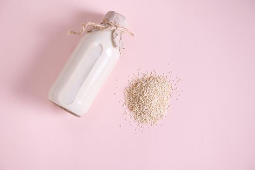 Heap of white rice and bottle of plant based organic healthy rice milk on pink surface. Vegan wholesome dairy free drink