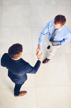 Its a pleasure to welcome you to our company. High angle shot of two businessmen shaking hands in an office.