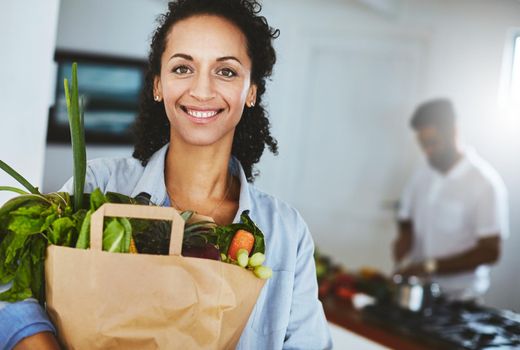 Living healthy and living well. Portrait of a happy woman holding a bag of fresh vegetables while standing in her kitchen.
