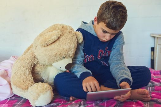 Teddy is just as curious about technology. a young boy using a digital tablet at home.