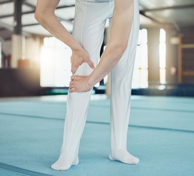 Gym, sport and injury of a professional gymnast suffering from leg pain or ache during training indoors. Sore knee, legs and muscle from intense athletic practice or workout exercise for competition.