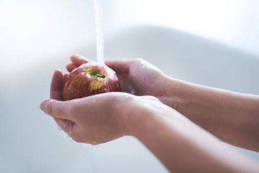 Almost ready to eat. a person washing an apple at a tap.