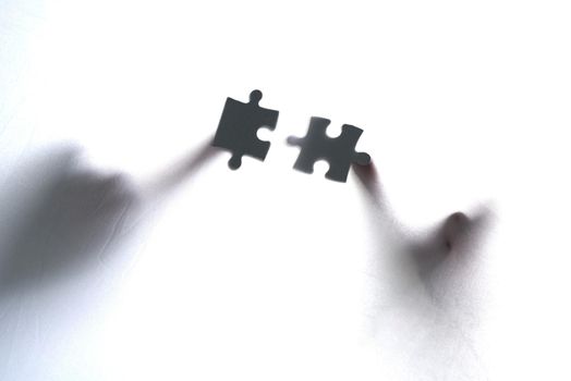 Fitting the pieces together. two unrecognizable people holding two puzzle pieces together.