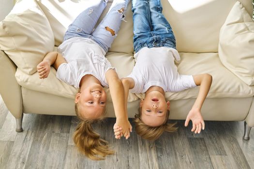 Pretty little girl and boy are lying on sofa in living room