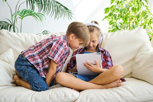 Cute kids with headphones enjoying tablet at home.