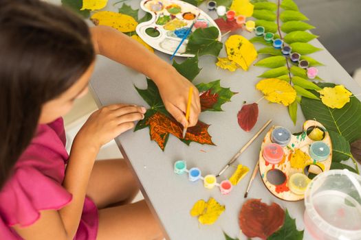 Little girl painting on autumn yellow leaves with gouache, kids arts, children creativity, autumn art. High quality photo