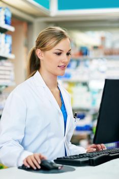 Keeping a close eye on her customers records. a young pharmacist using a computer at the checkout counter.