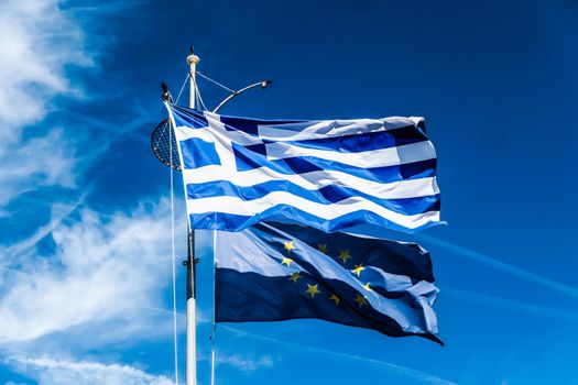 Flags of Greece and European Union on blue sky background, politics of Europe