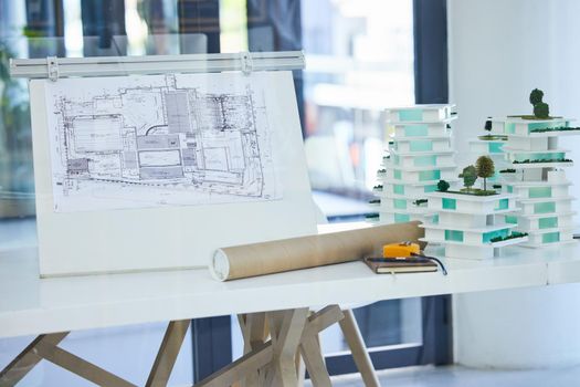 Architecture, design and blueprints on an office desk with plans and a building model for the construction industry. Architect office, planning and equipment in a modern and creative workplace