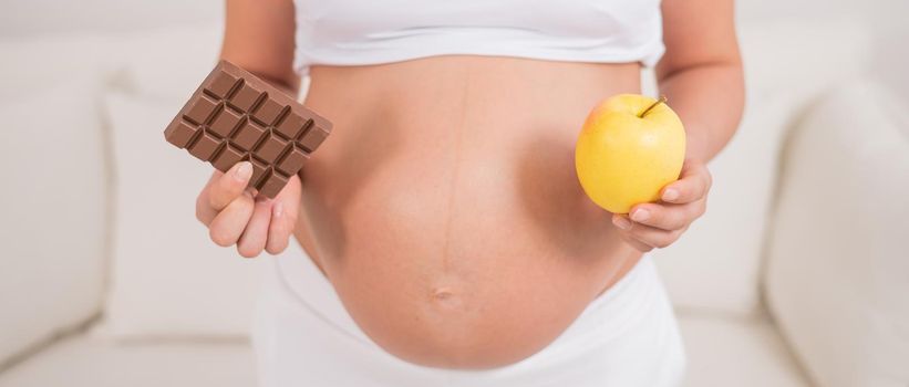 A pregnant woman is holding an apple and a bar of chocolate. The ninth month of pregnancy.