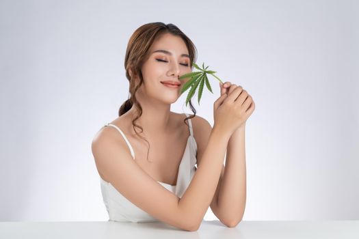 Gorgeous female model with healthy fresh skin and cosmetic holding hemp leaf.