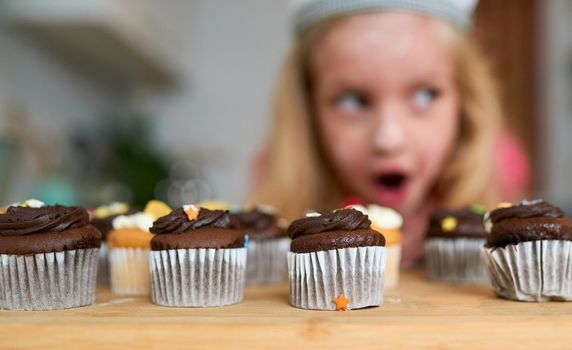 I cant believe I made these. a surprised little girl looking at cupcakes she baked at home.