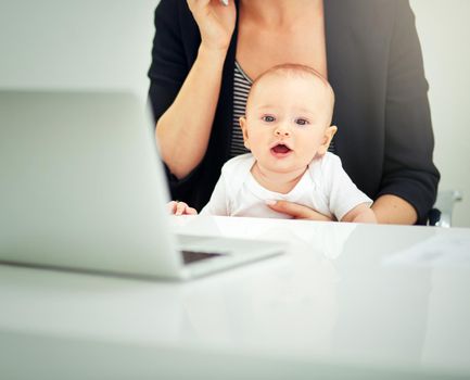 Looks like Im skipping school and getting straight to business. a businesswoman looking after her baby boy while working on her laptop.
