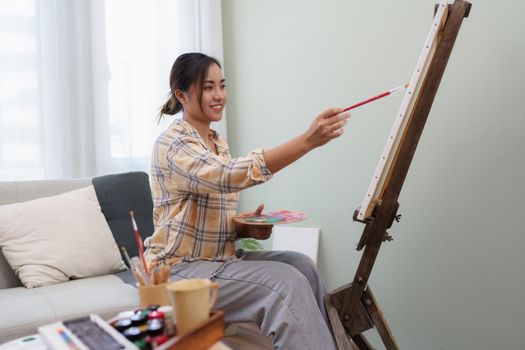 Joyful young female artist painting on canvas at workshop