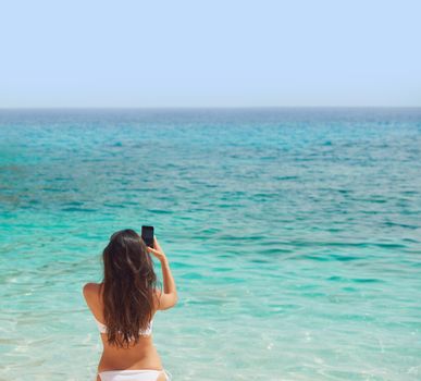 Beautiful woman taking photos with smart phone technology on paradise beach destination summer wanderlust vacation