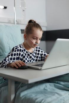 Ill kid resting on patient bed while enjoying gaming on modern computer