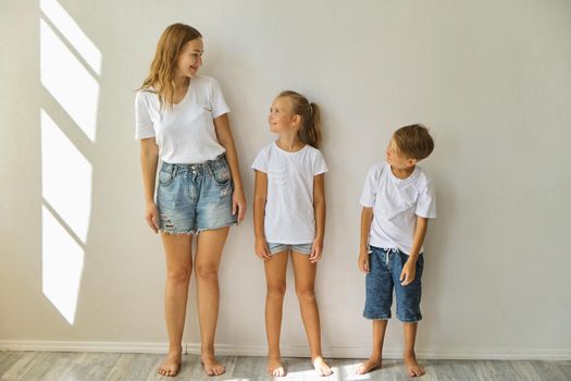 mother measures growth of kids to a daughter and son near light grey wall