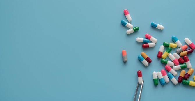 Antibiotic drug selection. Multi-colored capsule pills on blue background. Forceps picks a red-white capsule up from many antibiotic capsule pills. Chance of being selected. Probability sampling.