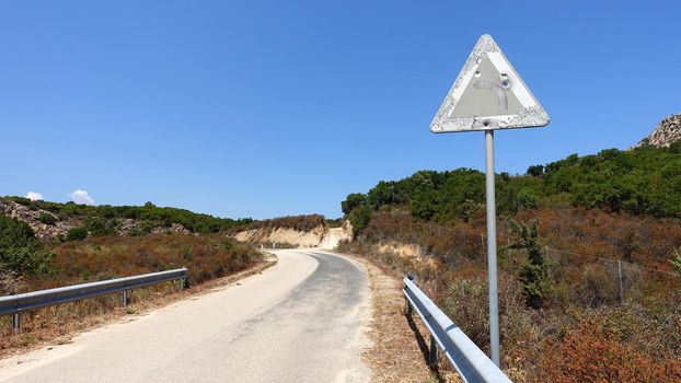 An old road sign indicating a dangerous curve, perhaps riddled with rifle shots.