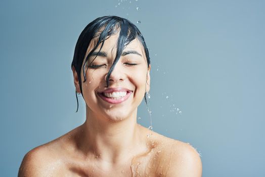 Cleanliness is next to happiness. a young woman having a refreshing shower against a blue background.