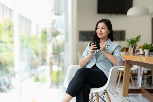 Beautiful asian businesswoman in elegance suit sitting at office desk and holding a coffee cup. Female entrepreneur, business owner.