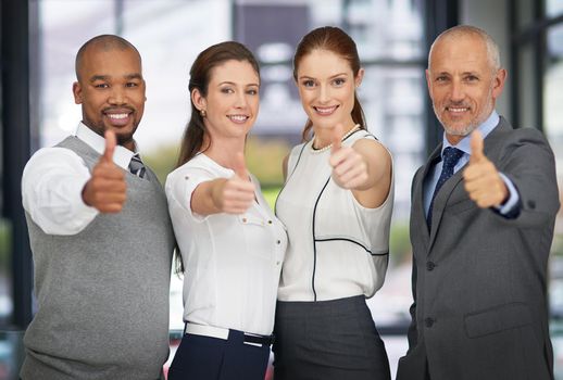 Were on it. Portrait of a group of businesspeople pulling thumbs up while standing in the office.