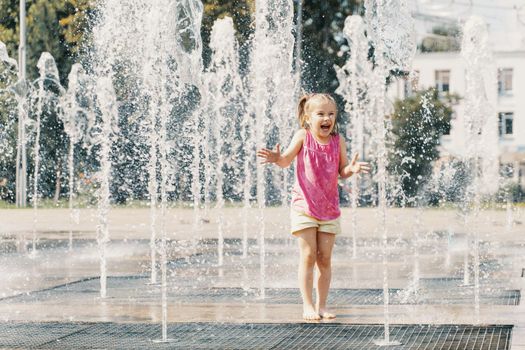 child girl playing in the water jets of the fountain
