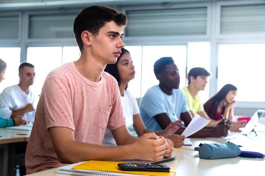 Caucasian teen male high school student in class. Multiracial university students in classroom. Copy space