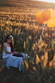 Nature is a source of unending inspiration. a cute little girl playing with a typewriter while sitting in a cornfield.