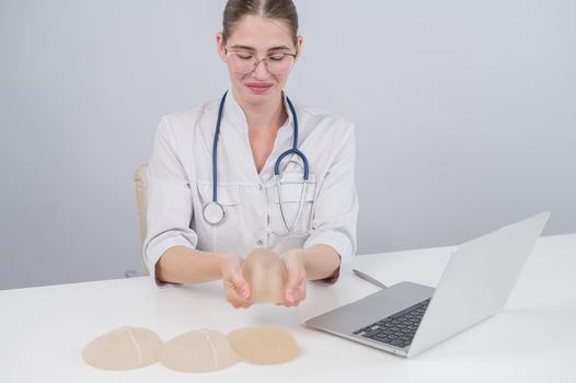 Woman plastic surgeon demonstrating breast implants at her desk.