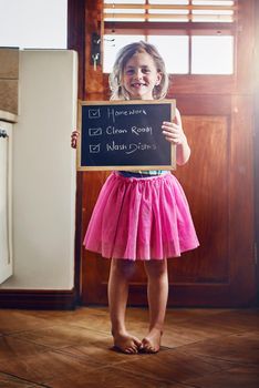All her chores are done and dusted. Portrait of a little girl holding a chalkboard with chores written on at home.