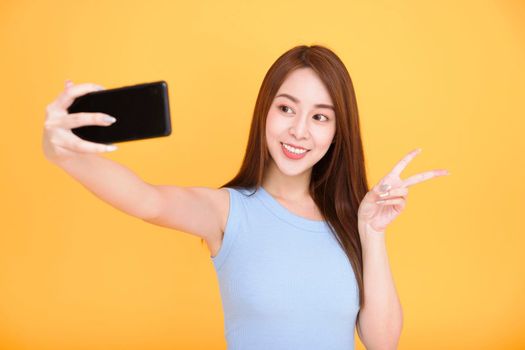 Young woman smiling and taking selfie photo onsmartphone isolated over yellow background
