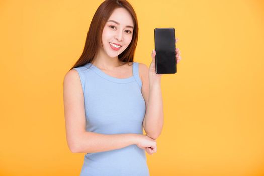 Smiling asian woman showing mobile phone screen on yellow background