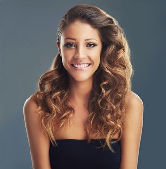 This hairstyle suits me perfectly. a beautiful woman with long brown curls posing against a grey background.