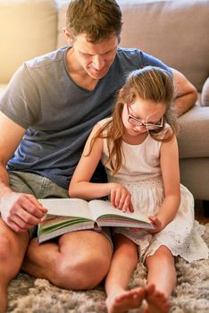 Whats this word, Dad. a father and his little daughter reading a book together at home.