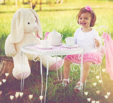 Cute as a button at tea time. a cute little girl having a tea party with her stuffed animal on the lawn outside.