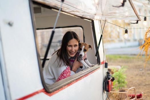 Caucasian woman looks out of the window of the van while hugging her dog Jack Russell Terrier. Travel in a camper in autumn.